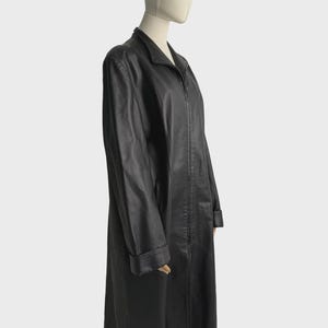 May include: A long, black leather coat with a collared neckline and a full-length zipper. The coat has long sleeves and a tailored fit, displayed on a mannequin.