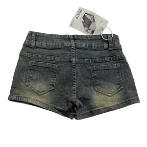 May include: Back view of denim shorts in a faded gray wash. The shorts have two back pockets and a waistband with belt loops. A tag with the text "JIANYU" is attached to the shorts.