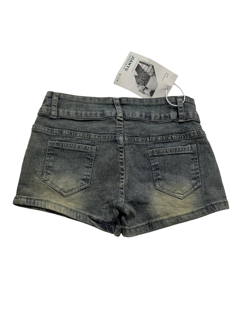 May include: Back view of denim shorts in a faded gray wash. The shorts have two back pockets and a waistband with belt loops. A tag with the text "JIANYU" is attached to the shorts.