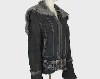 May include: A black jacket with a gray faux fur collar and trim. The jacket features a front zipper closure, white contrast stitching, and a wide belt at the waist with a metal buckle. The sleeves have adjustable buckled straps at the cuffs.