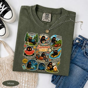 Może przedstawiać: Oliwkowozielony t-shirt z nadrukiem graficznym przedstawiającym małe czarne stworzenia podczas letnich zajęć. Tekst zawiera Summer Vibes, Hammock Chill, Tie-Dye Club, Garden Guardian, Watermelon Rush, Route 66 Explorer, River Adventure, Firefly Gatherer oraz Starry Nights.