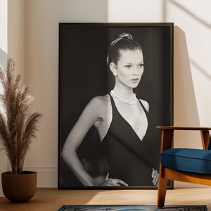 Può includere: Un ritratto in bianco e nero incorniciato di una donna in abito nero, appoggiata a un muro. Un tappeto blu con un bordo decorativo è sul pavimento in legno. Una sedia blu e una pianta in vaso sono anche nella stanza.