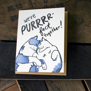 May include: A greeting card with a blue and white illustration of two cats cuddling. The card reads "we're purrrfect together!"