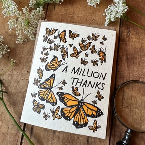 May include: A white card with a brown border features a design of orange butterflies with black outlines. The text "A MILLION THANKS" is printed in black at the center of the card.