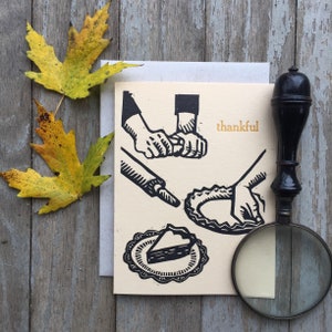 May include: A card with a black and white illustration of hands making a pie crust. The card has the word "thankful" printed in gold lettering.