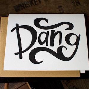 May include: A white card with a black and white illustration of the word "Dang" in a stylized font.