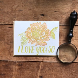 May include: A white card with a yellow and peach flower illustration and the text "I LOVE YOU SO".