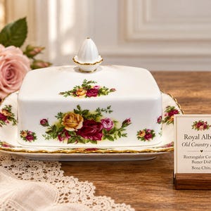 May include: A white bone china rectangular covered butter dish featuring the Royal Albert Old Country Roses floral pattern with red, yellow, and pink roses, green leaves, and gold trim. The lid has a white finial and the base has scalloped edges.