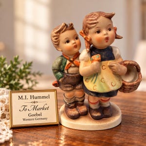 Puede incluir: Una figura de porcelana de dos niños de pie juntos, con la niña sosteniendo una cesta. Una placa rectangular junto a la figura muestra el texto: M.I. Hummel, To Market, Goebel, Western Germany. Los niños visten ropa tradicional.