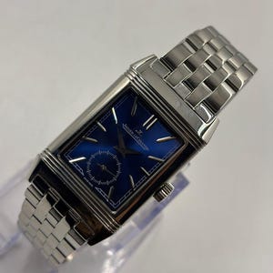 Peut inclure: Une montre-bracelet rectangulaire avec un cadran bleu et des aiguilles et index argentés. La montre dispose d'un petit sous-cadran des secondes et est sertie dans un boîtier argenté avec un bracelet à maillons assorti.