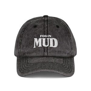 Puede incluir: Gorra de béisbol negra desgastada con visera curva. La gorra presenta el texto blanco "FOKIN MUD" en la parte delantera. El sombrero tiene un aspecto vintage y desgastado.