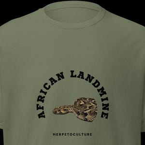 Puede incluir: Camiseta verde oliva con un gráfico de serpiente y el texto "AFRICAN LANDMINE" en semicírculo sobre la serpiente, y "HERPETOCULTURE" debajo. El gráfico de la serpiente está detallado con patrones marrones y beige.