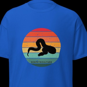 Könnte beinhalten: Königsblaues T-Shirt mit einer schwarzen Schlangensilhouette vor einem Sonnenuntergangsdesign mit orangefarbenen, roten und gelben Streifen. Der Text "HERPETOCULTURE" steht darunter.