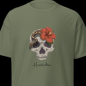 May include: Olive green t-shirt featuring a skull with a snake and a red hibiscus flower. The text "Herpetoculture" is written in a cursive font below the skull. The shirt is a short-sleeved, crew neck style.