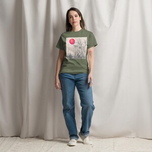 Może przedstawiać: Oliwkowa koszulka z kwadratową grafiką przedstawiającą czerwone słońce i bambus. Koszulka jest połączona z niebieskimi dżinsami i białymi trampkami. Na grafice widnieje napis "BALANCE LIFE".