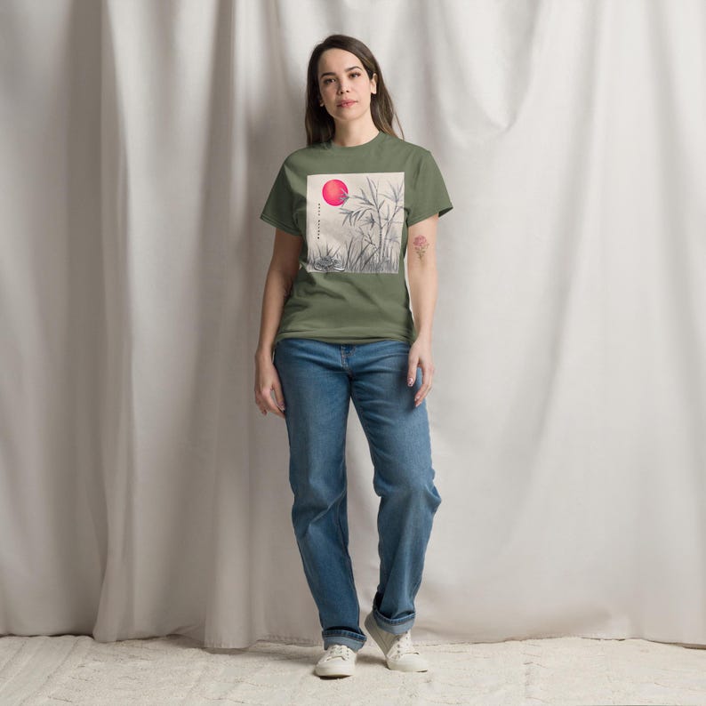 Może przedstawiać: Oliwkowa koszulka z kwadratową grafiką przedstawiającą czerwone słońce i bambus. Koszulka jest połączona z niebieskimi dżinsami i białymi trampkami. Na grafice widnieje napis "BALANCE LIFE".