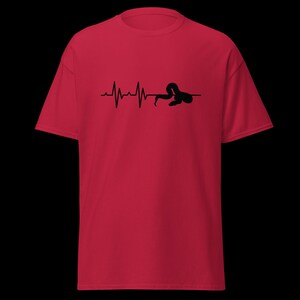 May include: A red t-shirt with a black graphic depicting a heartbeat line ending with a snake. The snake is coiled and integrated into the heartbeat design. The shirt has a crew neck and short sleeves.