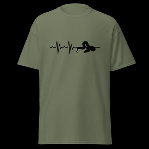 May include: An olive green t-shirt with a black graphic depicting a heartbeat line morphing into a snake. The design is centrally placed. The shirt has short sleeves and a round neck.