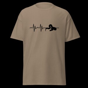 May include: A tan t-shirt with a black graphic depicting a heartbeat line ending with a snake. The snake is coiled and integrated into the heartbeat design. The shirt is made of a soft material and has short sleeves.