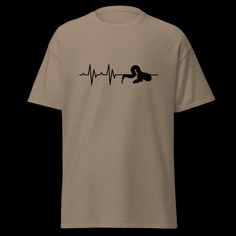 May include: A tan t-shirt with a black graphic depicting a heartbeat line ending with a snake. The snake is coiled and integrated into the heartbeat design. The shirt is made of a soft material and has short sleeves.