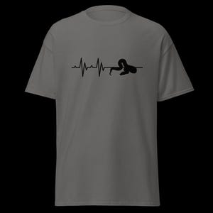 May include: Grey t-shirt with a black graphic depicting a heartbeat line morphing into a snake silhouette. The design is centrally placed. The shirt has short sleeves and a crew neck.