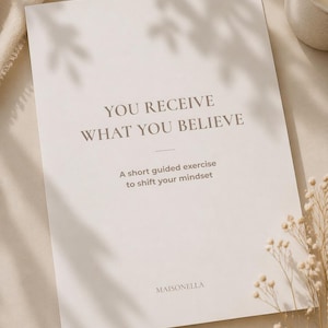 May include: A cream-colored booklet with the text "YOU RECEIVE WHAT YOU BELIEVE" and "A short guided exercise to shift your mindset." The booklet is branded with the name "MAISONELLA". The image has a soft, neutral aesthetic.