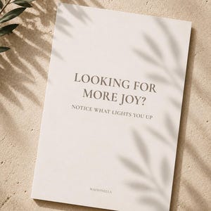 Puede incluir: Una tarjeta rectangular de color blanco hueso con el texto gris oscuro LOOKING FOR MORE JOY? NOTICE WHAT LIGHTS YOU UP y el nombre de la marca MAISONELLA en la parte inferior. La tarjeta tiene una superficie lisa y un diseño claro.