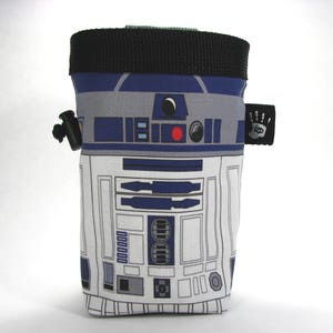 Peut inclure: Un sac à craie d'escalade bleu et blanc avec un motif R2-D2. Le sac a un cordon de serrage noir et une sangle noire avec une petite étiquette noire.