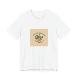 Puede incluir: Camiseta blanca con un gráfico de una planta en maceta con el texto "I love you so much I could sip". La planta es verde con hojas rizadas, y la maceta es marrón. Una regadera y una paleta también están en el gráfico.