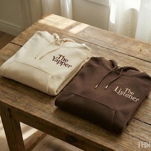Peut inclure: Un sweat à capuche crème avec le texte The Yapper en marron et un sweat à capuche marron foncé avec le texte The Listener en crème. Les deux sweats possèdent une poche kangourou, une capuche avec cordons assortis et des manches longues.