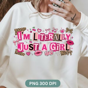 以下が含まれることがあります： ピンクと黒のブロック文字で「I'M LITERALLY JUST A GIRL」と書かれた白いスウェットシャツ。ヒョウ柄、さくらんぼ、ハート、リボン、唇がアクセントになっています。デザインは装飾的な要素に囲まれています。