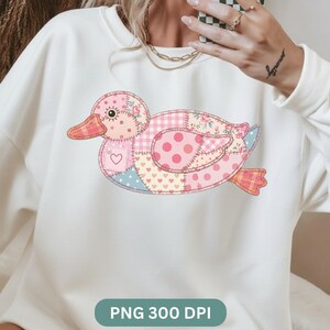 May include: White sweatshirt featuring a patchwork duck design in pink, blue, and yellow. The duck has a heart, floral, and polka dot patterns. The text "PNG 300 DPI" is at the bottom of the image.