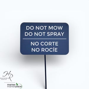 May include: A dark blue rectangular sign on a black stake. The sign reads "DO NOT MOW DO NOT SPRAY" in white text, with "NO CORTE NO ROC&Iacute;E" below. The sign is for a garden or lawn.