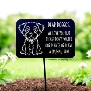May include: A black rectangular garden stake with a white cartoon dog illustration and text that reads "DEAR DOGGOS. WE LOVE YOU BUT PLEASE DON'T WATER OUR PLANTS OR LEAVE A GRUMPIE. THXI". The stake is in a garden.