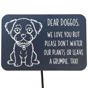 Black aluminum sign with an engraved cartoon dog and humorous message: 'Dear Doggos, we love you but please don't water our plants or leave a grumpie. Thx!' Designed for pet-friendly gardens and respectful dog walking.