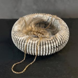 May include: A decorative, round bowl with a textured, ridged exterior in shades of grey and white. A gold-coloured chain necklace rests inside the bowl. The text "Roseley Creations" is visible on the bowl.