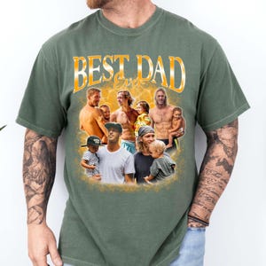 May include: An olive green short-sleeve t-shirt featuring a graphic print with the text "BEST DAD Ever" in yellow. The design includes a collage of multiple photographs showing various fathers and children in a warm, golden-toned background.