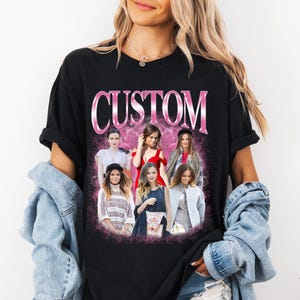 May include: A black short-sleeved t-shirt featuring the word CUSTOM in large pink metallic letters at the top. Below the text is a collage of six different photographs of individuals in various outfits, set against a pink, cloudy background.