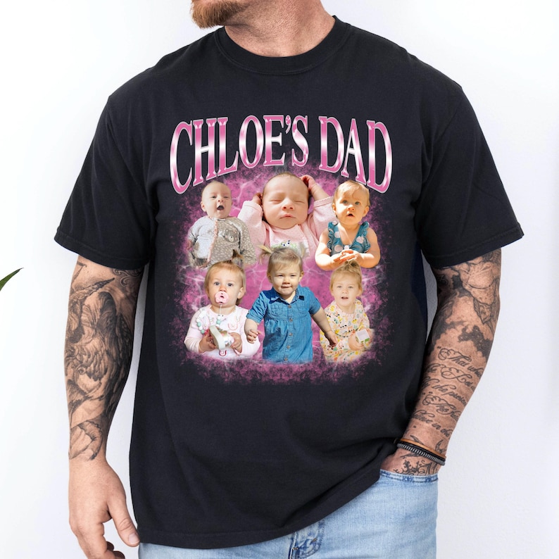 May include: A black short-sleeved t-shirt featuring the text CHLOE'S DAD in pink metallic-style lettering above a collage of six photographs of a young child. The photos are set against a pink, cloud-like background on the front of the shirt.