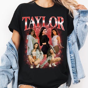 May include: A black t-shirt featuring the word TAYLOR in large red metallic-style letters at the top. Below the text is a collage of five photographs of a person in various poses and outfits, set against a red, smoky, and textured background.