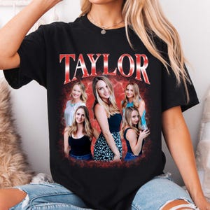May include: A black short-sleeve t-shirt featuring a graphic print with the word TAYLOR in large red metallic-style letters. Below the text are five photographic images of the same person in various outfits against a red smoky background.