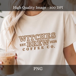 Può includere: Una t-shirt a maniche corte color crema con testo marrone che recita WITCHES BREW EST. 1626 COFFEE CO. La maglia presenta un girocollo e una vestibilità standard, con la grafica centrata sul petto in un carattere serif con contorno.