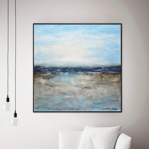 May include: Abstract painting of a seascape with blue and brown hues. The painting depicts a horizon with a blue sky and a brown beach with a blue ocean in the distance. The painting is framed in a black frame and is hanging on a white wall.