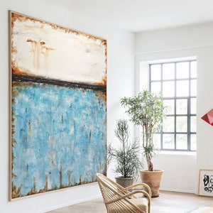 May include: Abstract painting with a blue, white, and brown color scheme. The painting is hanging on a white wall in a room with a wooden floor and a wicker chair.