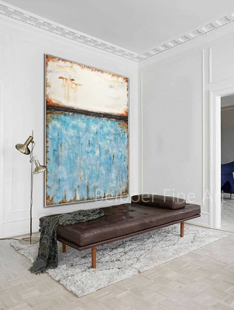 May include: Abstract painting with a blue, white, and brown color scheme. The painting is hanging on a white wall above a brown leather daybed with a white rug.
