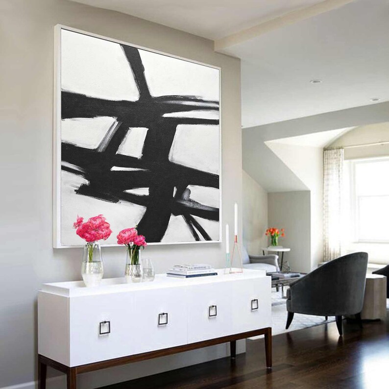 May include: A large black and white abstract painting with bold brushstrokes hangs above a white dresser with four drawers. The painting is framed in a thin white frame.
