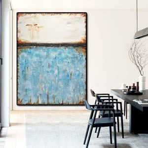 May include: Abstract painting with a blue and white color scheme. The painting is framed in a black frame and hangs on a white wall. The painting is in a living room setting with a wooden table and chairs.
