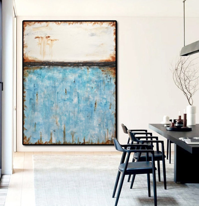 May include: Abstract painting with a blue and white color scheme. The painting is framed in a black frame and hangs on a white wall. The painting is in a living room setting with a wooden table and chairs.