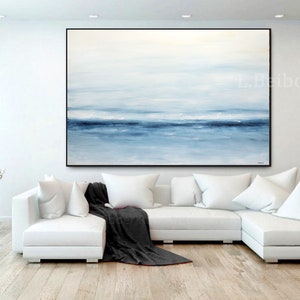 May include: A large abstract painting of a seascape in shades of blue and white hangs above a white sectional sofa in a modern living room.
