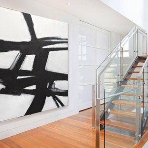 May include: Abstract black and white painting on a white canvas. The painting features bold black lines and shapes against a white background. The painting is hanging on a white wall in a modern home.